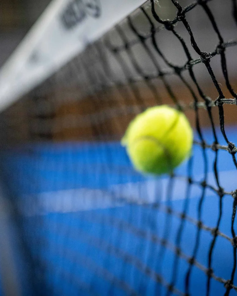 Padelball fliegt knapp über das Netz auf blauem Padelplatz